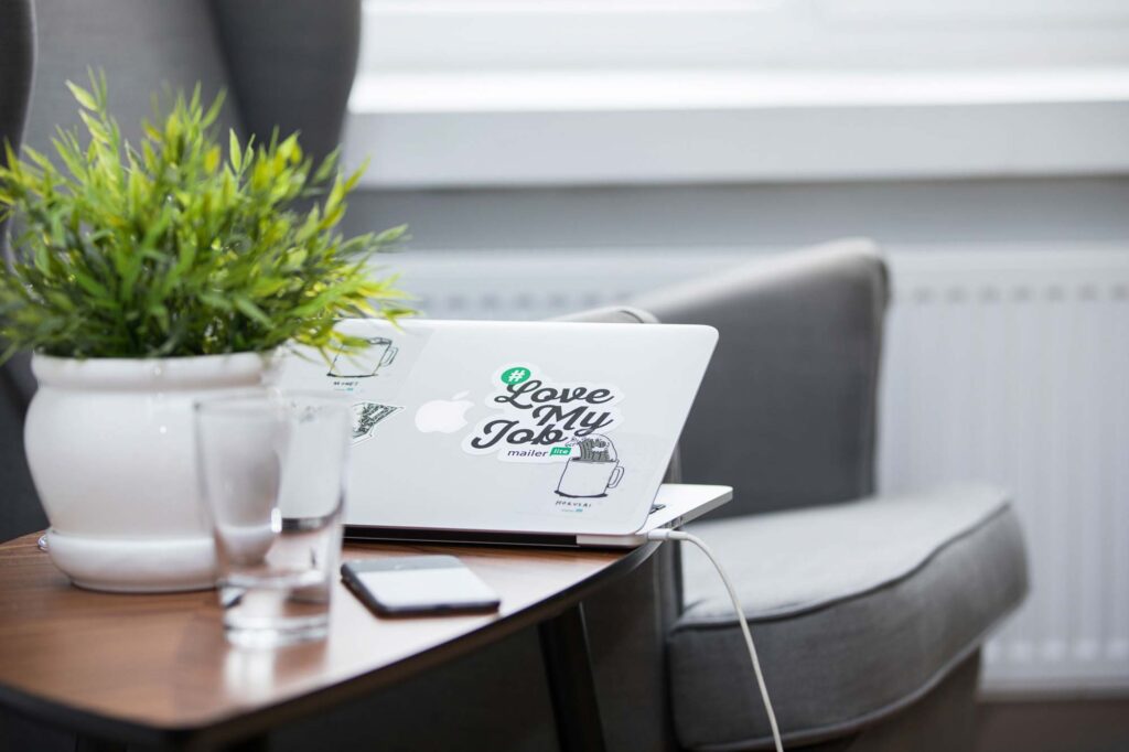 A laptop lef ton a small coffe table, partially open with a sticker that says 'I love my job'